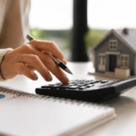 Hands using calculator with small house model representing Charlotte real estate financial decisions in spring 2026
